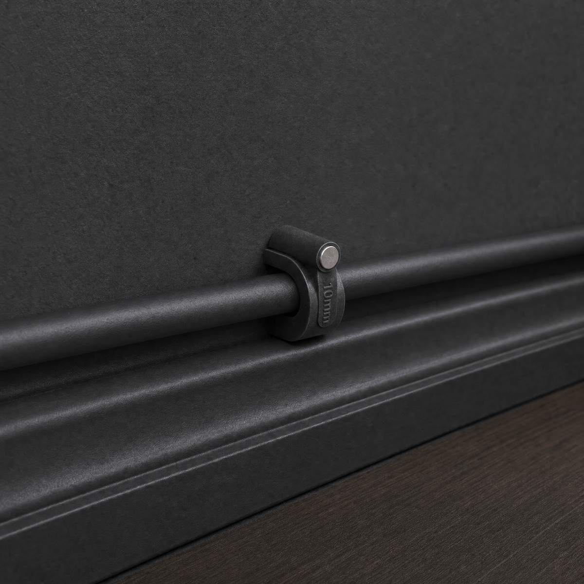 QualGear 10 mm cable clip in black mounted on a black wall, nail driven straight into the surface