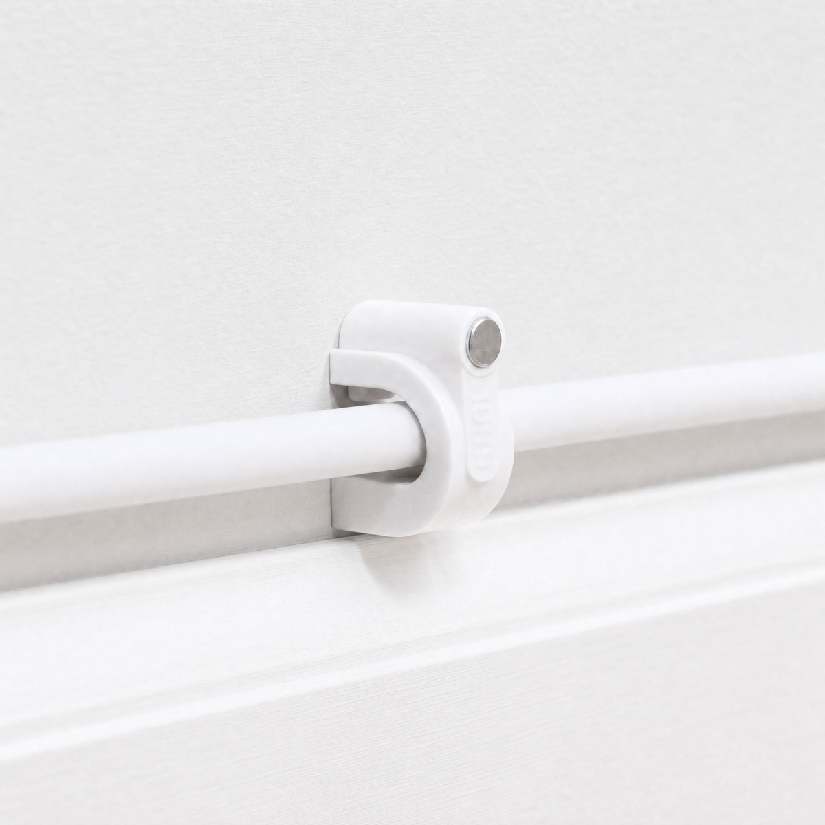QualGear 10 mm cable clip in white holding a white cable in a straight run along a white wall