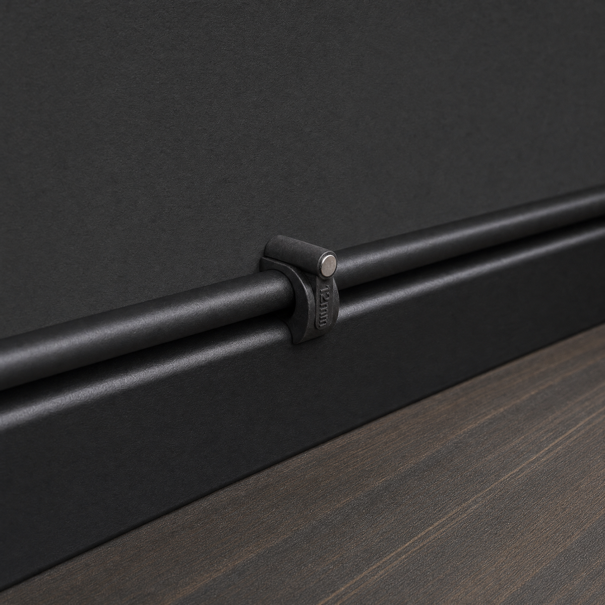 QualGear 12 mm cable clip in black, the largest size, securing a cable along a black wall