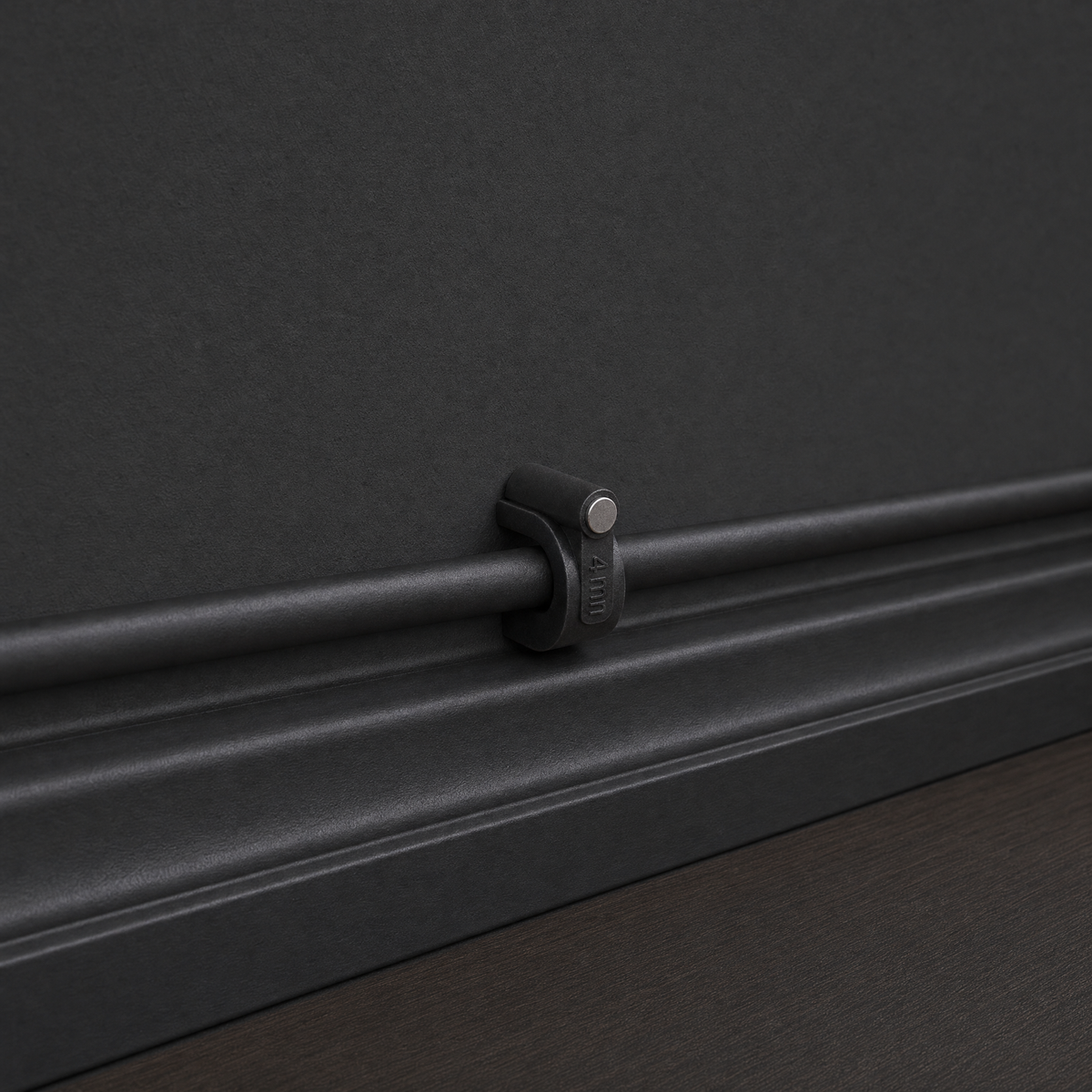 QualGear 4 mm cable clip in black, the smallest size, mounted flush on a black wall and baseboard