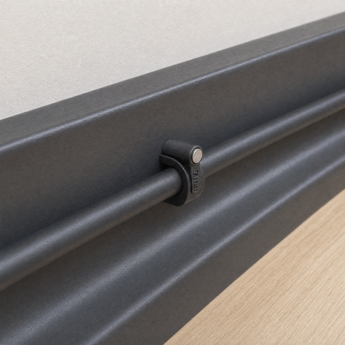 QualGear 7 mm cable clip in black securing a cable along a dark wall, nail set front-to-back