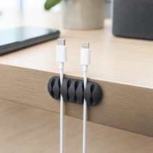 QualGear cable clip holder in black mounted on a desk edge, guiding two cables from a charger
