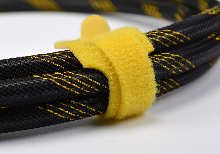 Yellow QualGear reusable tie gripping a braided cable bundle, opened and re-wrapped by hand-free fabric